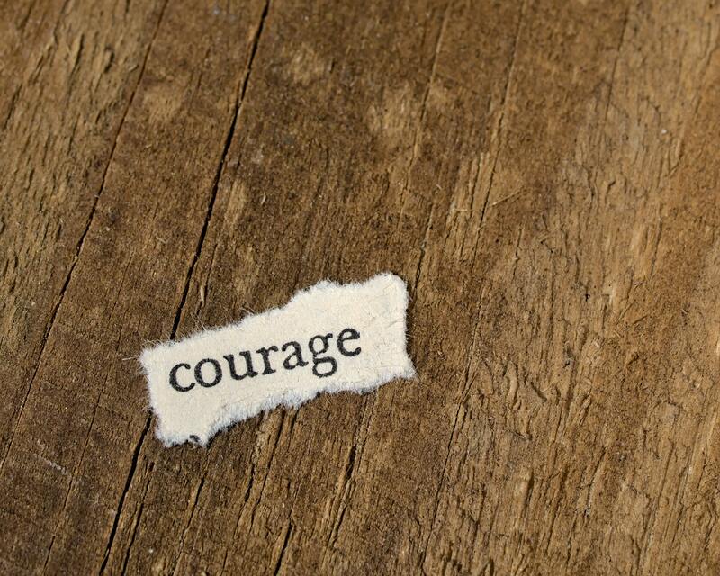 a torn piece of paper on a wooden background that says courage
